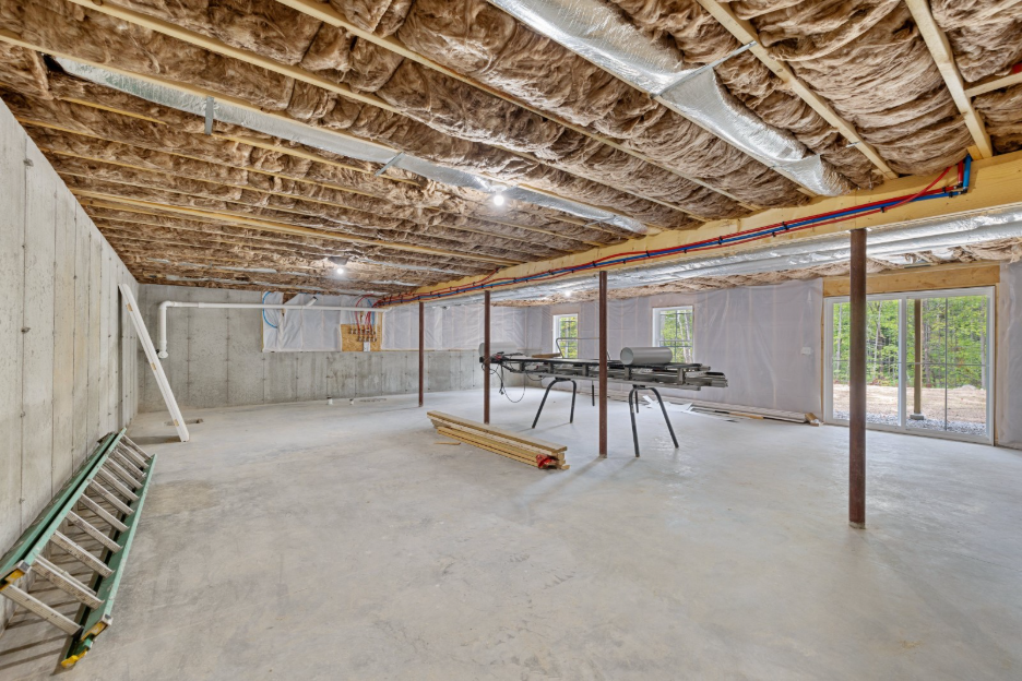 Unfinished basement with exposed insulation, HVAC ductwork, support posts, concrete flooring, and construction materials awaiting renovation.